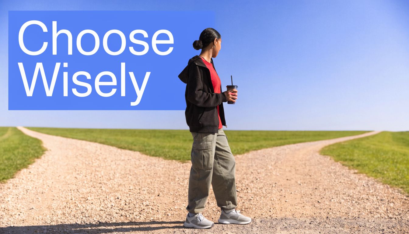 A person standing at a fork in a dirt road in a field under a clear sky.